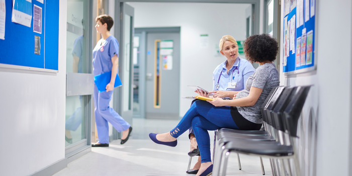 uma médica loira sentada no corredor conversando de forma bem calma com sua paciente